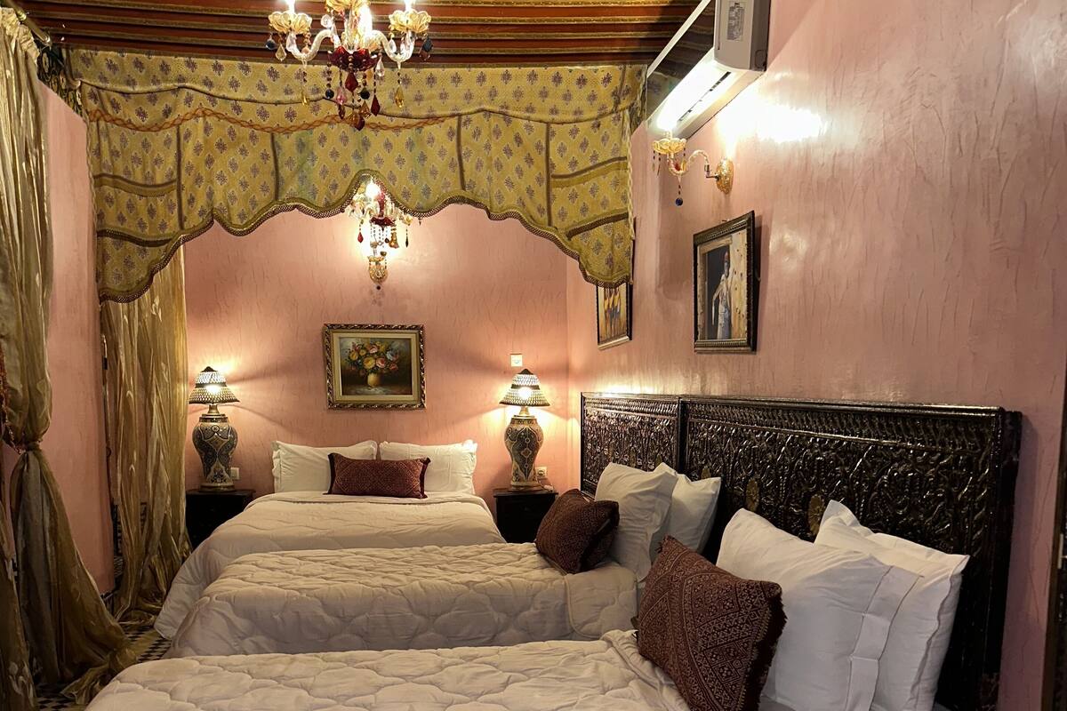 Une chambre avec deux lits, un lustre, des rideaux à motifs et un sol à carreaux.
