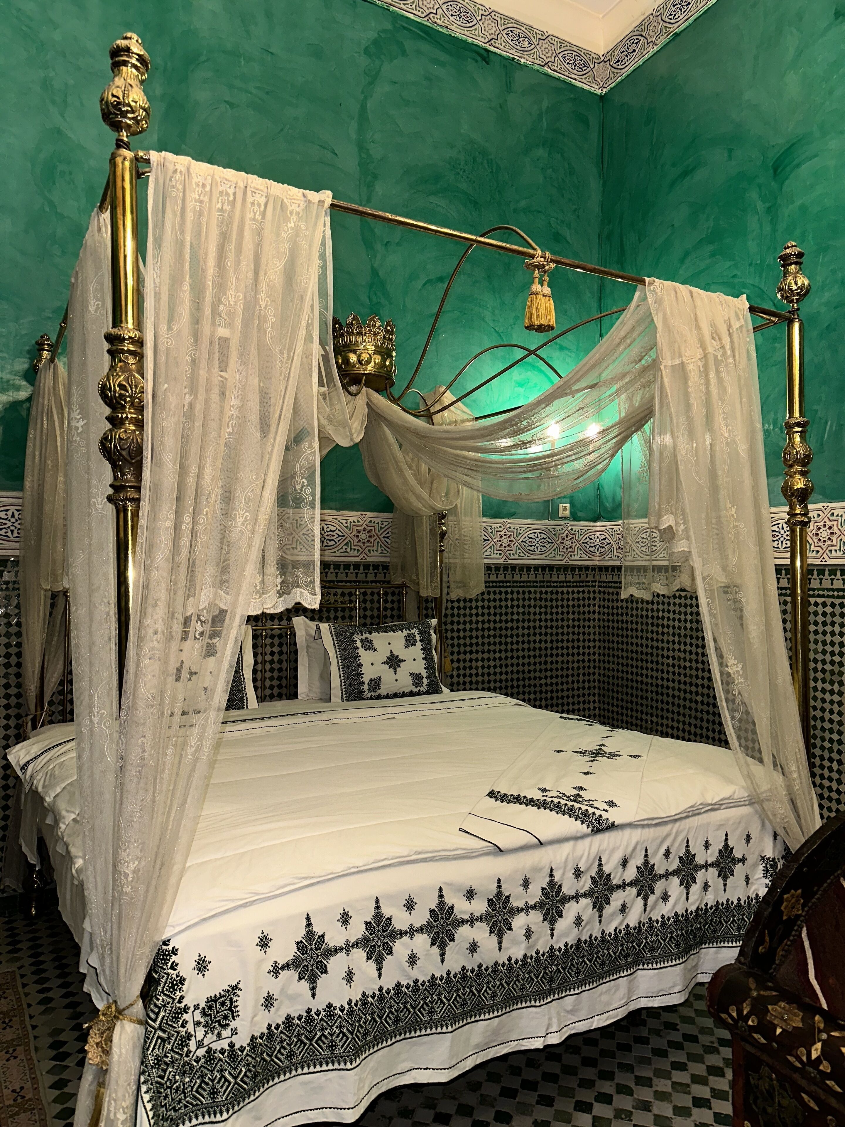 Una cama con dosel, un dosel con cortinas, una corona decorativa y un suelo a cuadros.