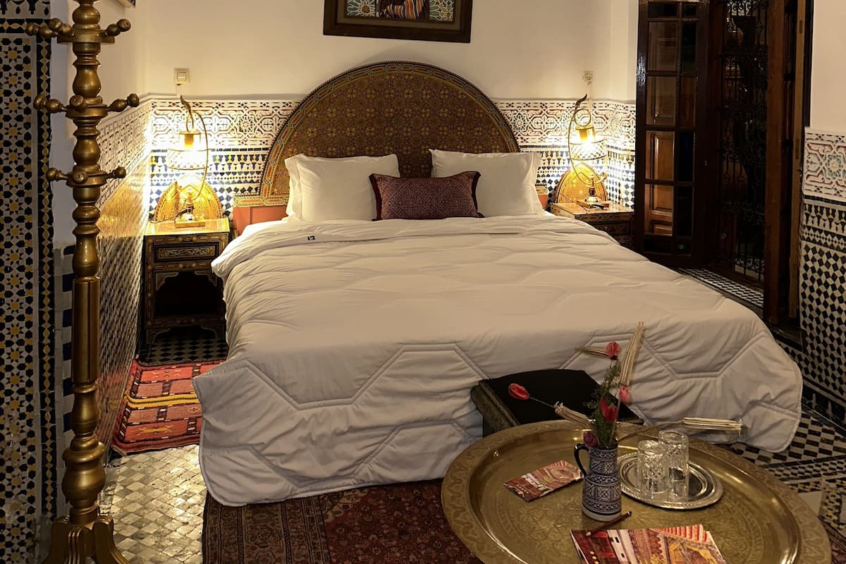 Une pièce traditionnelle marocaine comprenant un lit, une décoration murale, un tapis à motifs et une petite table avec un plateau.