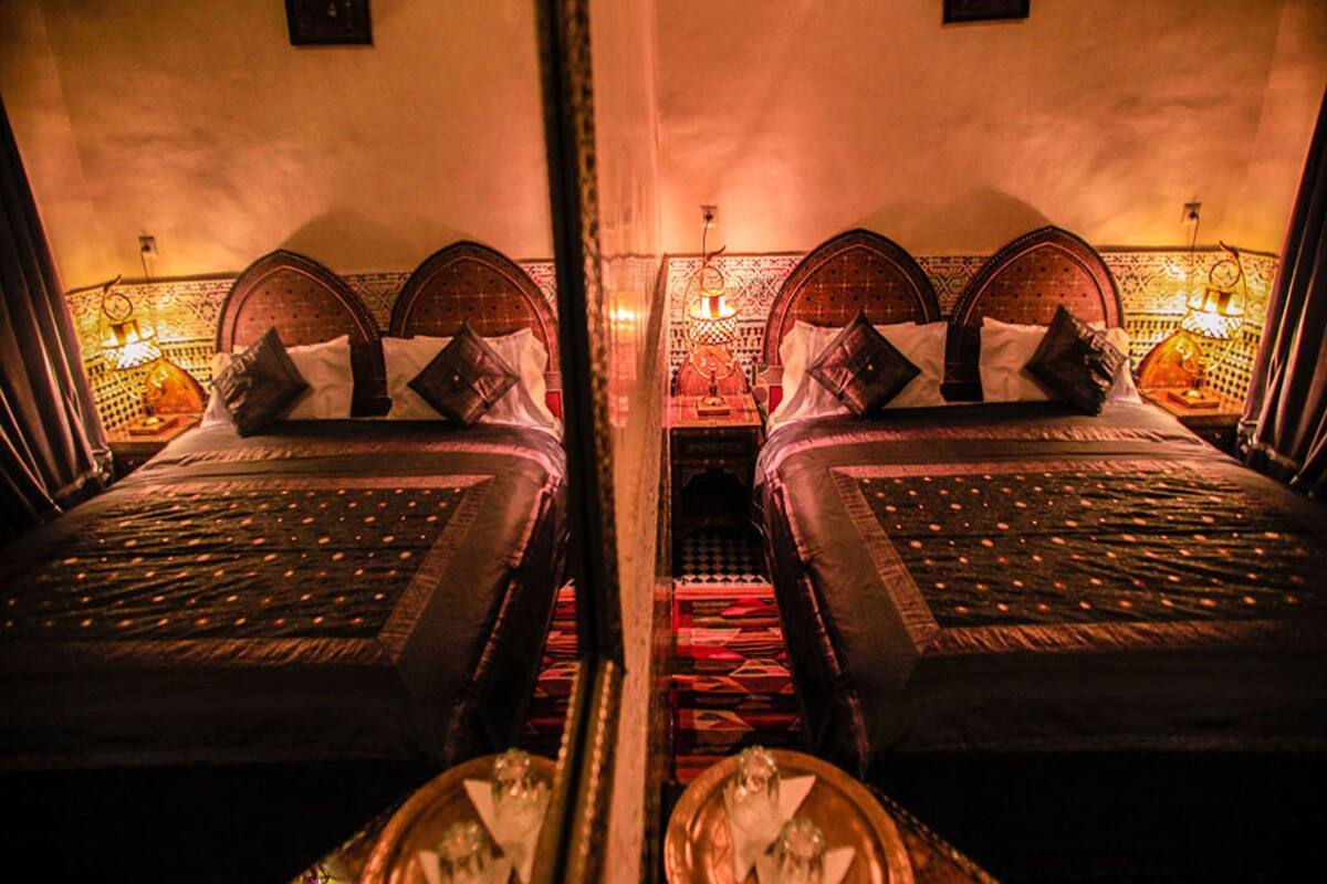 Une vue en miroir d’une pièce avec deux lits, chacun doté d’une tête de lit et d’une table de chevet avec une lampe.