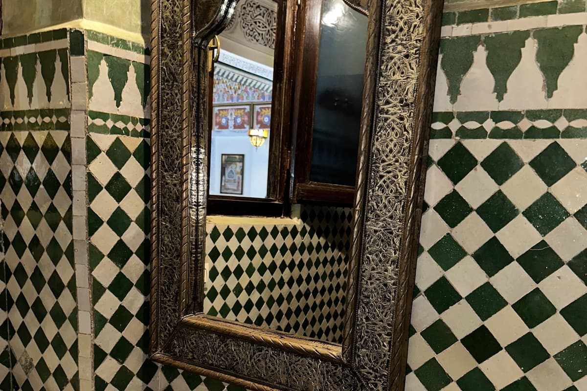 Une salle de bain avec un sol carrelé à motifs, un lavabo en cuivre, un miroir doté d’un cadre orné et une serviette.