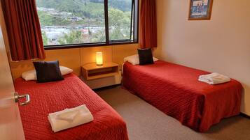Habitación de hotel con dos camas, una mesita de noche, una lámpara, una ventana con cortinas y un cuadro en la pared.