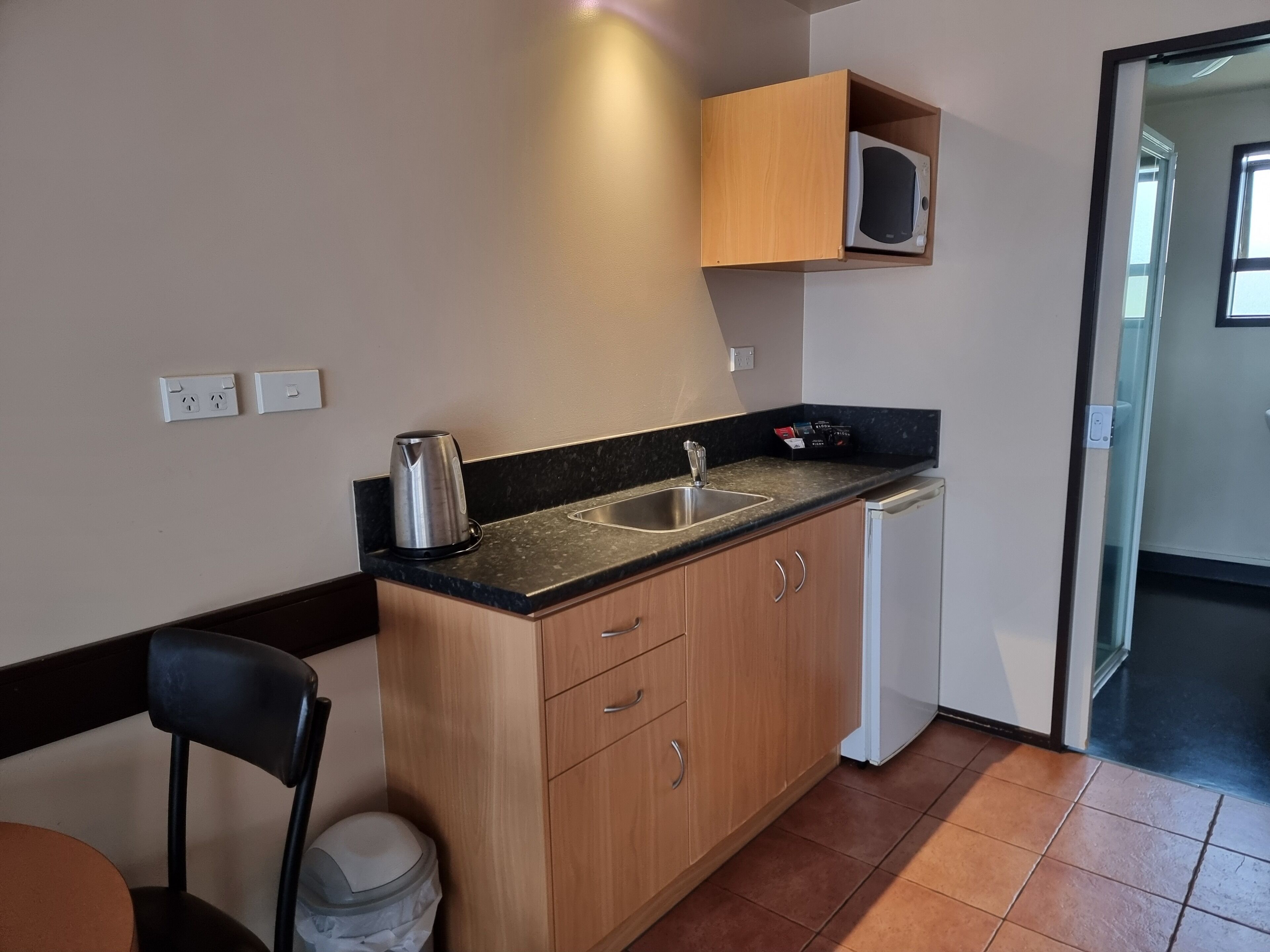 A compact kitchen with a sink, a microwave, and a kettle on the countertop.