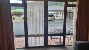 A hotel room with a sliding glass door leading to an outdoor area with a table and chairs. - Broadway Motel (Picton)