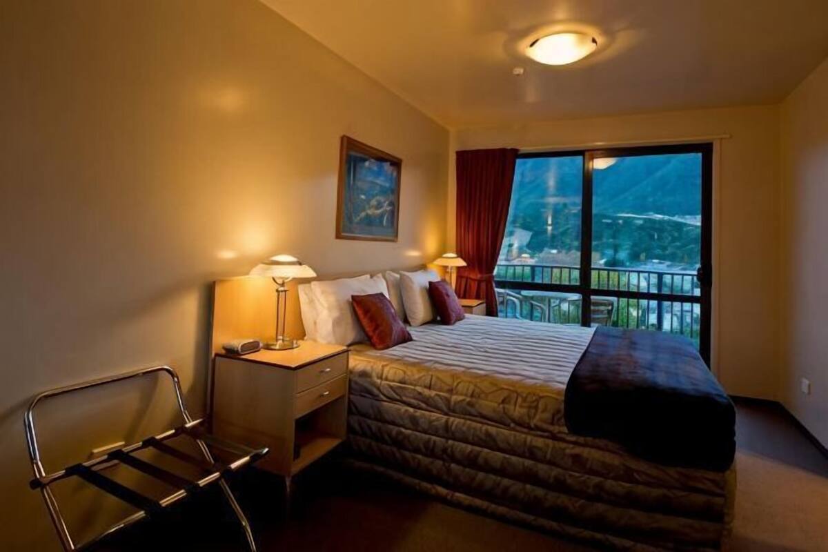 A bedroom with a bed, bedside lamps, a chair, a nightstand, and a large window with a view.