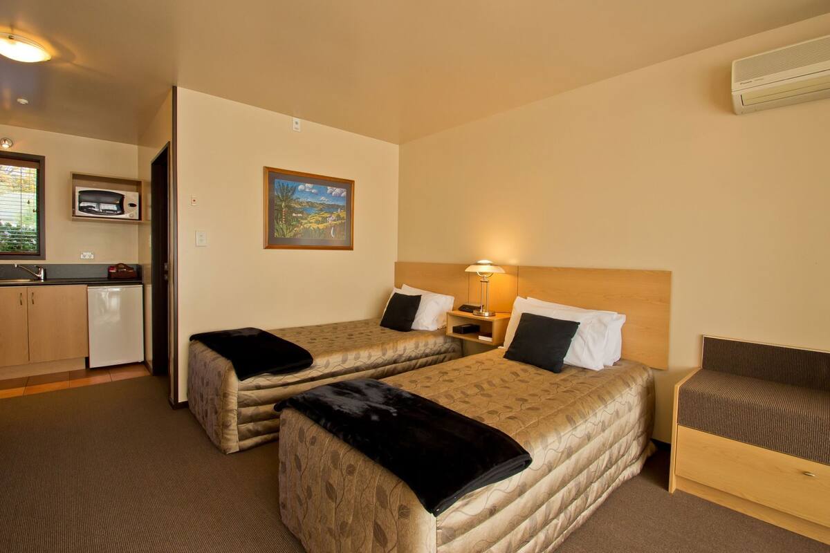 A hotel room with two beds, a desk, a microwave, and a small kitchenette.