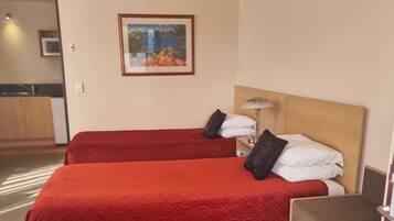 Una camera d'albergo con due letti, una testiera in legno, un comodino con una lampada e un quadro appeso al muro.