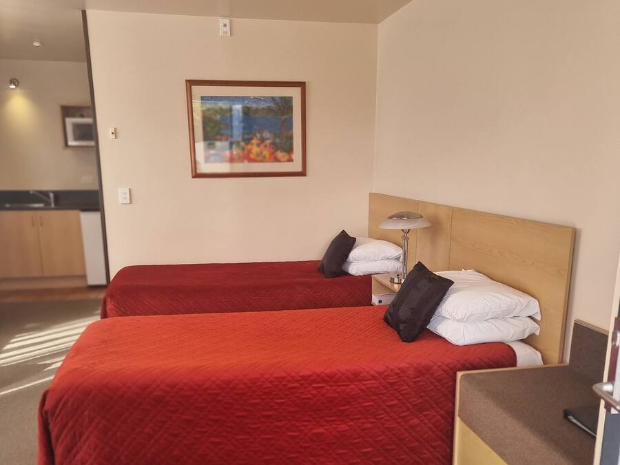Une chambre d’hôtel avec deux lits, une tête de lit en bois, une table de chevet avec une lampe et un tableau encadré au mur.