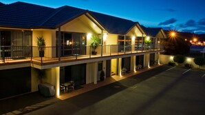 A hotel with a covered outdoor seating area, multiple balconies, and a parking lot. - Broadway Motel (Picton)