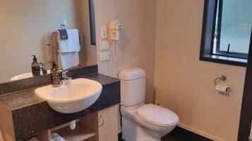 Ein modernes Badezimmer mit einem weißen Waschbecken, einer dunklen Arbeitsplatte und einer Toilette. Ein Fenster bietet einen Blick nach draußen, und ein Handtuchhalter trägt ein Handtuch.