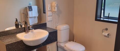 A modern bathroom with a white sink, dark countertop, and a toilet. There is a window with a view of the outside, and a towel rack with a towel hanging on it.