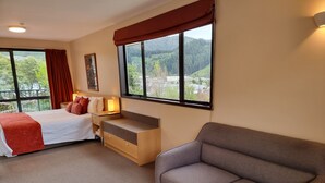 A hotel room with a bed, a sofa, a desk, and large windows offering a view of the outdoors. - Broadway Motel (Picton)