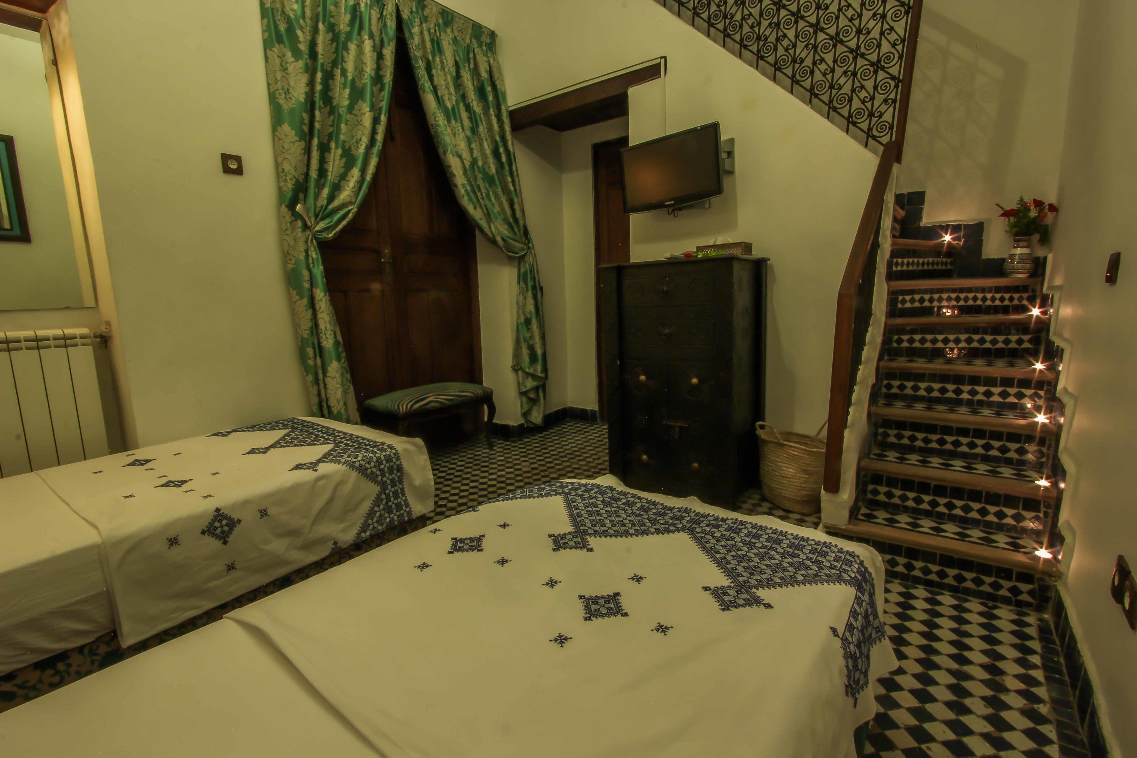 Una habitación con dos camas, un armario de madera, televisión y una escalera con azulejos decorativos.