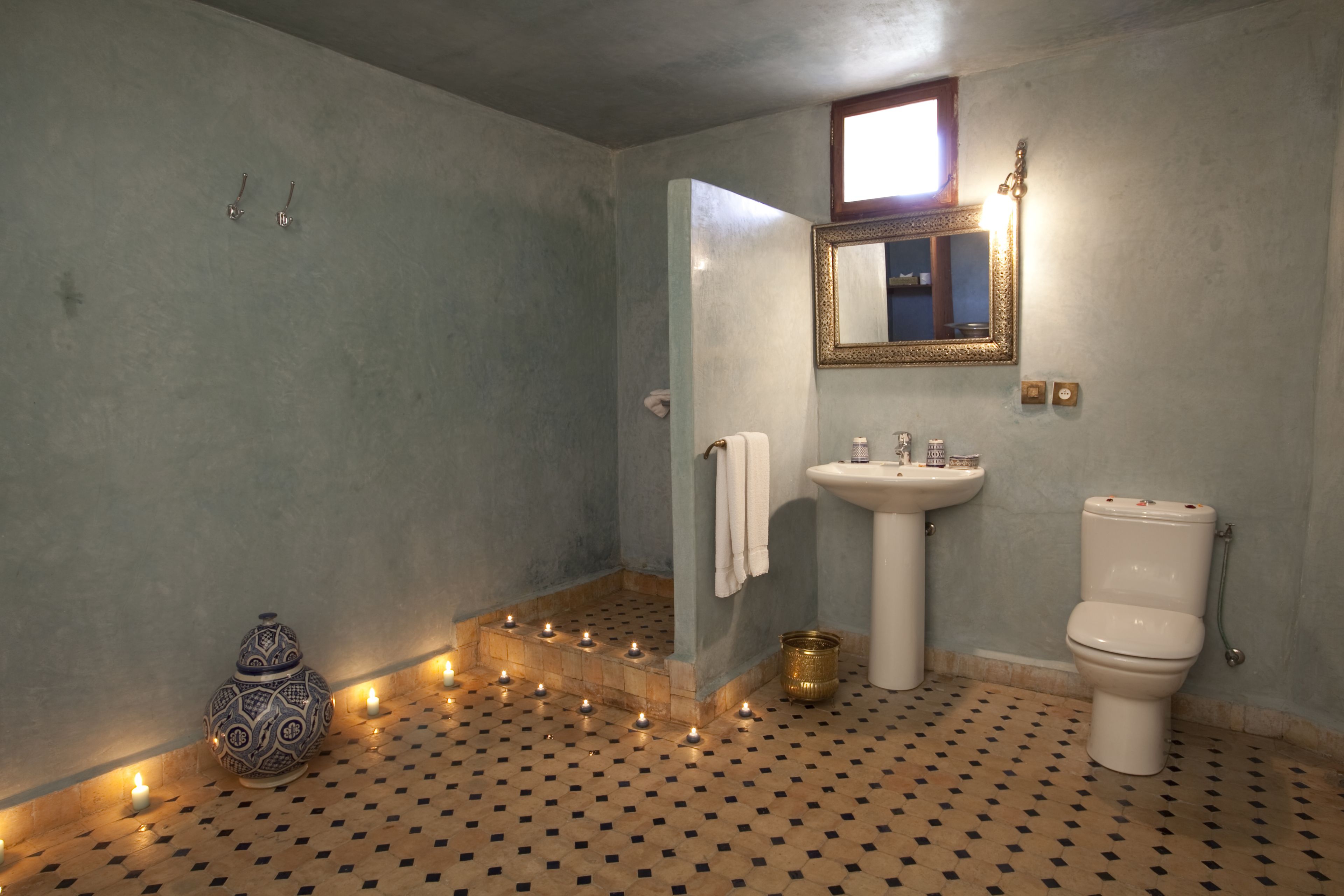 Un baño con suelo de baldosas, un lavabo, un inodoro, un espejo y velas.