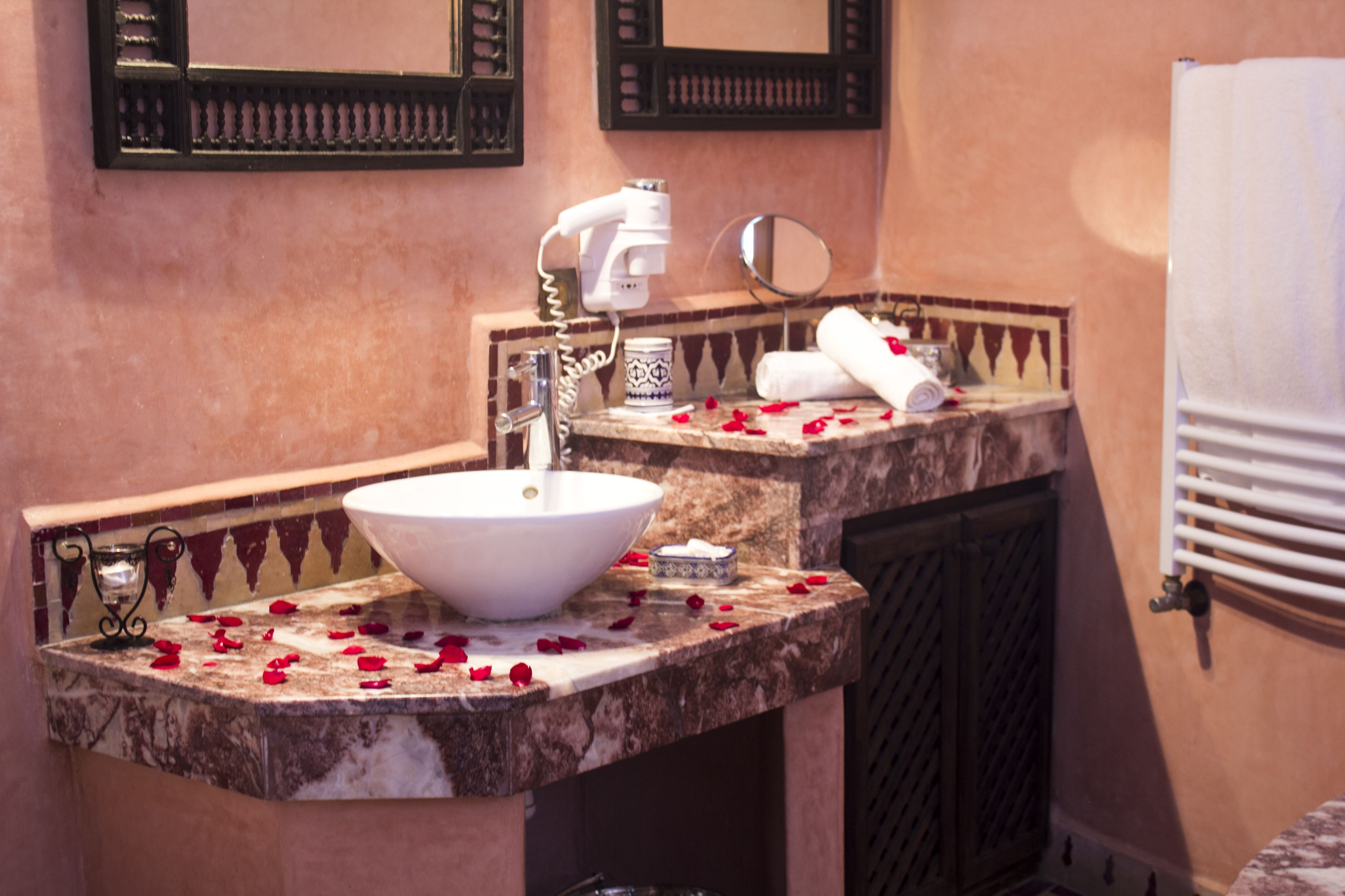 A bathroom with a marble sink, a hairdryer, a mirror, and a towel rack.