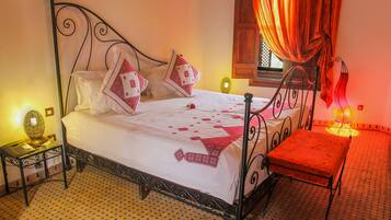 A neatly made bed with patterned pillows, a bedside table with a lamp, and a window with curtains.
