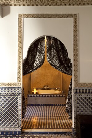 A room with a patterned floor, a bed with a headboard, and a small table with a candle.
