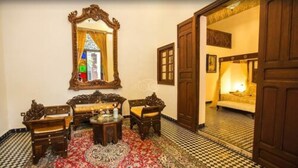 Une pièce au décor traditionnel, avec un sol à carreaux, un ensemble de meubles en bois, un miroir et une porte donnant sur une autre pièce.