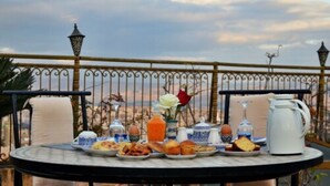 Une table dressée avec des aliments pour le petit-déjeuner, notamment des viennoiseries, des œufs et des boissons, sur un balcon offrant une vue sur le panorama de la ville.