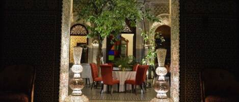 An indoor dining area with a table set for four, surrounded by ornate walls and a patterned floor.