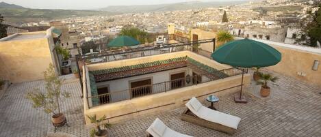 Eine Dachterrasse mit Liegestühlen und Sonnenschirmen, die einen Blick auf die Stadt bietet.
