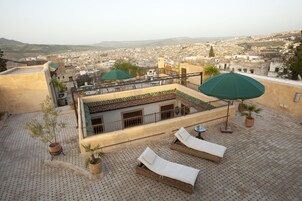 Terraço no telhado com espreguiçadeiras e guarda-sóis, com vista para a paisagem urbana.