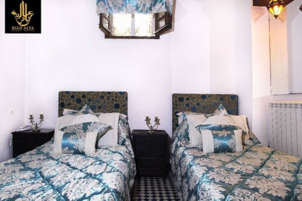 Une chambre avec deux lits, chacun doté d’une tête de lit à motifs et d’oreillers assortis. Une table de chevet avec une lampe se trouve entre les deux lits.