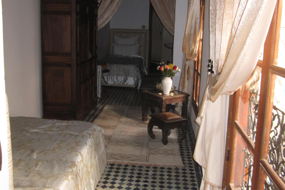 Une pièce comprenant un lit, une armoire en bois, une petite table avec un vase et une fenêtre avec des rideaux.