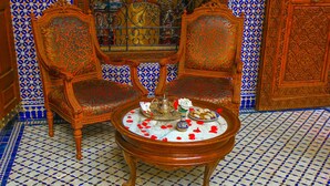 Une pièce dotée d’un sol à motifs, de deux fauteuils richement décorés, d’une table sur laquelle se trouvent une théière et des pâtisseries, et d’un mur décoratif orné de motifs complexes.