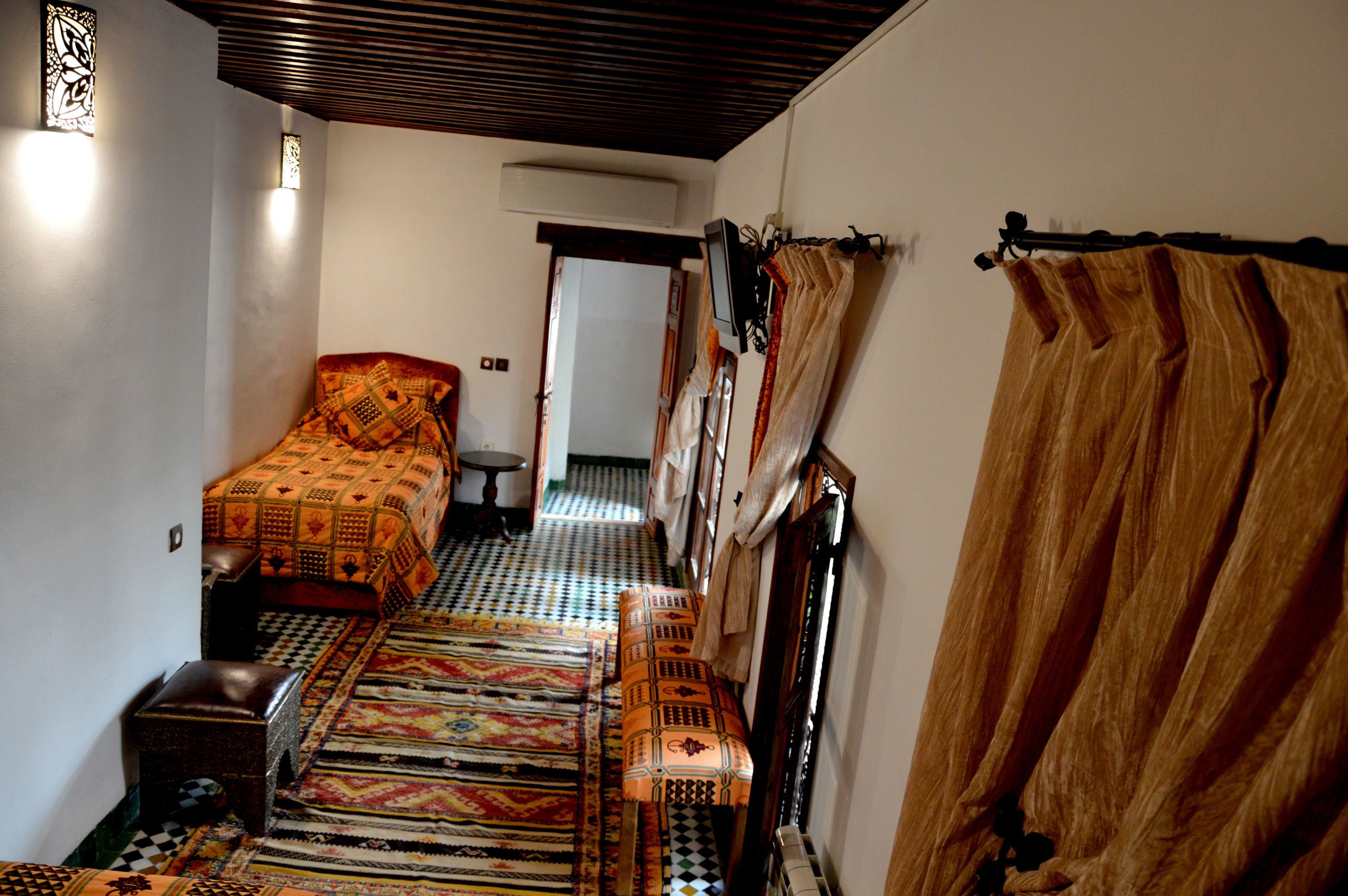 A narrow hallway with a patterned rug, a bench, and a bed with a patterned bedspread.