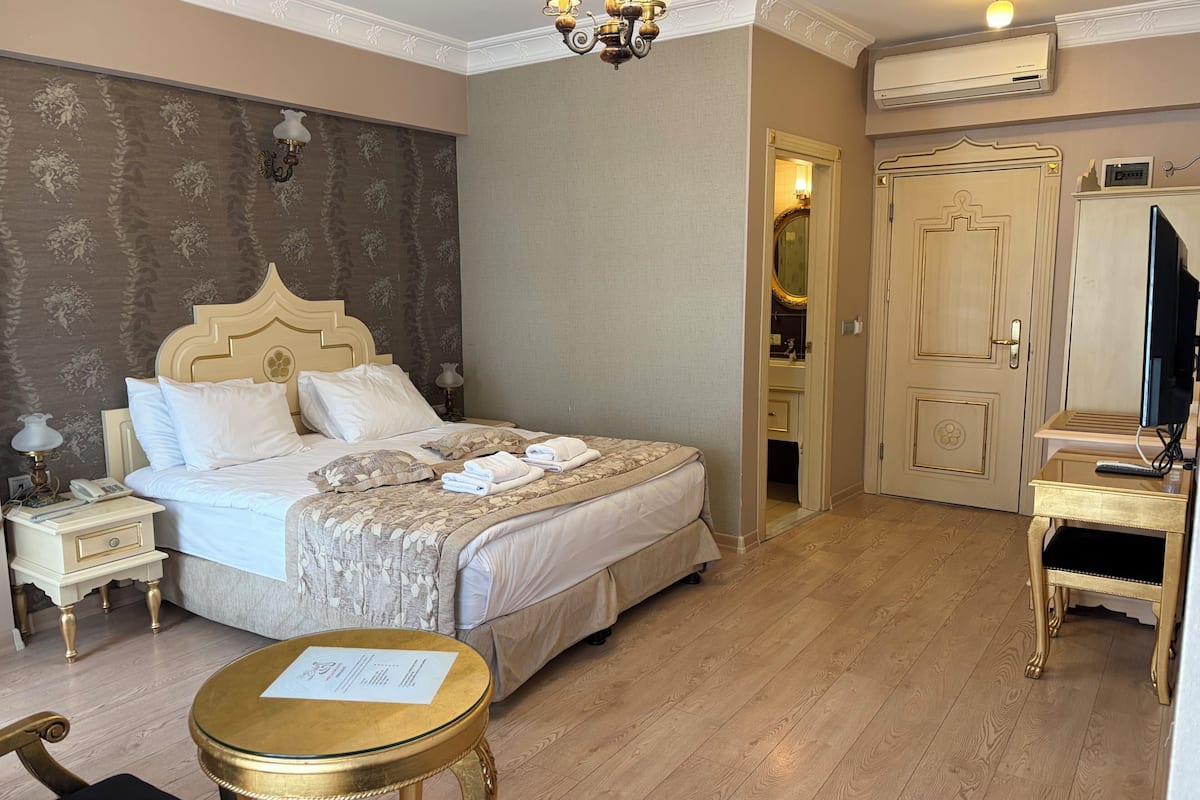 A hotel room with a bed, bedside table, lamp, chair, and a desk with a computer.