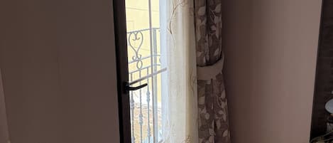 Una habitación con puerta de vidrio corredera que da a un balcón, una pequeña mesa blanca y una cortina estampada.