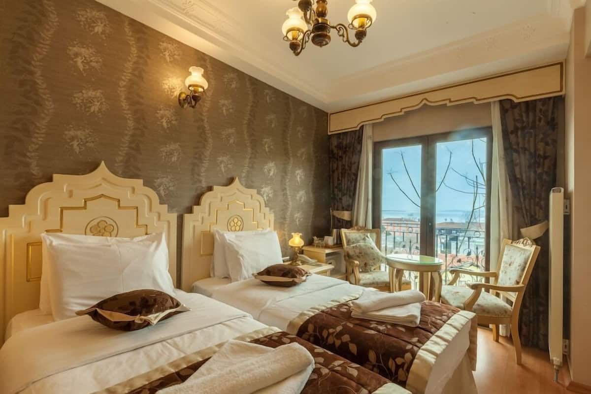 A hotel room with two beds, a chandelier, a balcony view, and a small table with chairs.