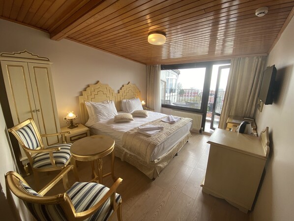 A hotel room with a large bed, two bedside tables, a small round table, a chair, a desk, and a TV on the wall.
