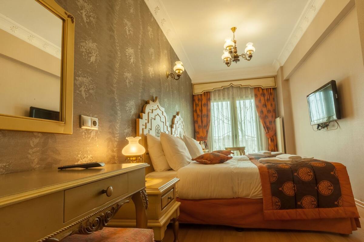 A hotel room with a bed, a dresser, a lamp, a TV, and a window with curtains.