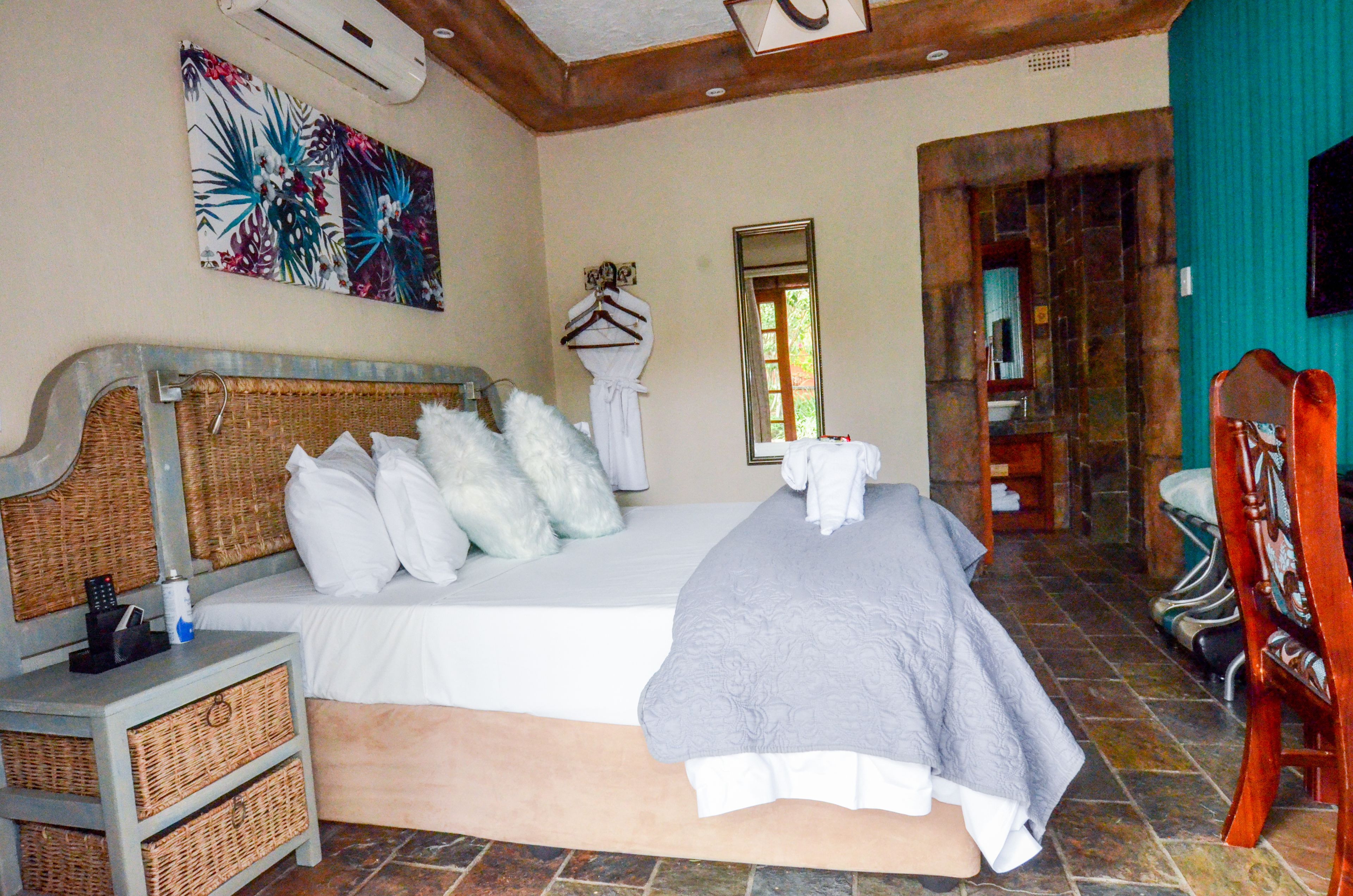 Een slaapkamer met een groot bed, een nachtkastje met een mand, een spiegel en een houten stoel.