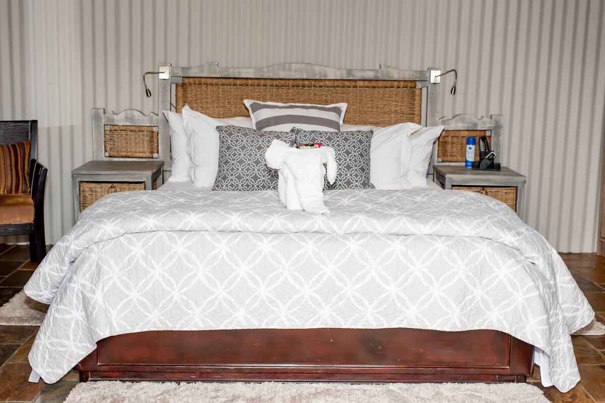 A neatly made bed with a white patterned bedspread, a wooden headboard, and two nightstands with a bottle and a remote control on one.