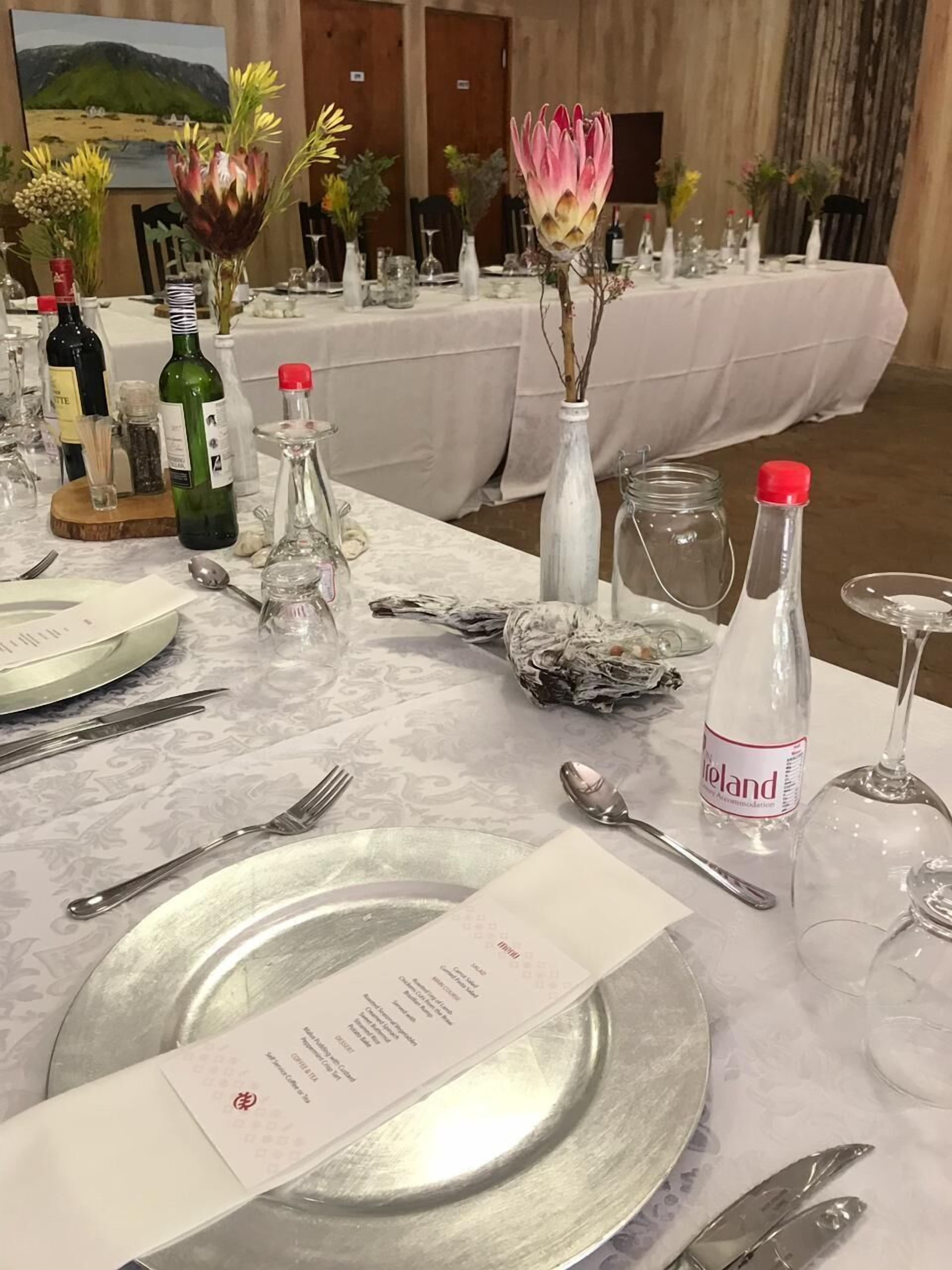 Une table mise pour un repas, avec un menu, des bouteilles de vin et des fleurs décoratives.