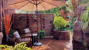 A patio area with a table and chairs under a large umbrella, surrounded by plants and rocks. - 61 On Ireland (Polokwane)