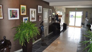 A lobby with a reception desk, framed artwork on the walls, a large potted plant, and a staircase leading to another floor. - Domaine du Griffier (Granzay-Gript)