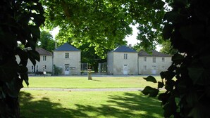 A courtyard with two stone buildings, a grassy lawn, and a tree providing shade. - Domaine du Griffier (Granzay-Gript)