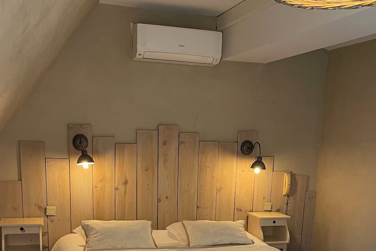 A bedroom with a large bed, wooden headboard, bedside lamps, and an air conditioning unit.