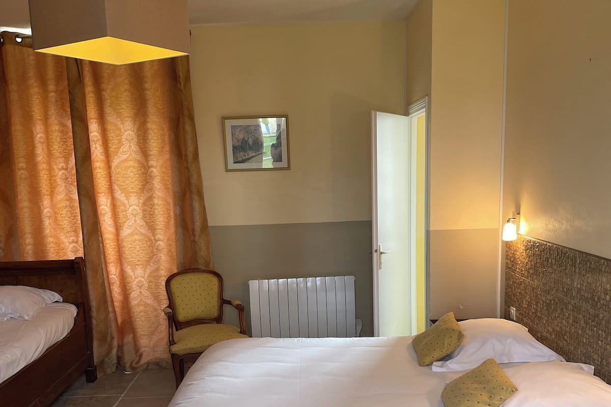 A hotel room with a large bed, a chair, a radiator, and a door.
