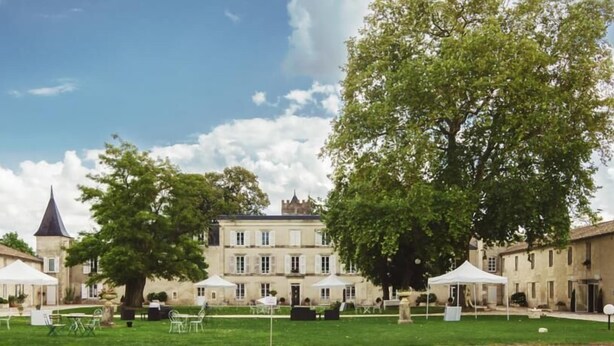 A courtyard with a large tree, a building with a tower, and outdoor seating areas. - Domaine du Griffier (Granzay-Gript)