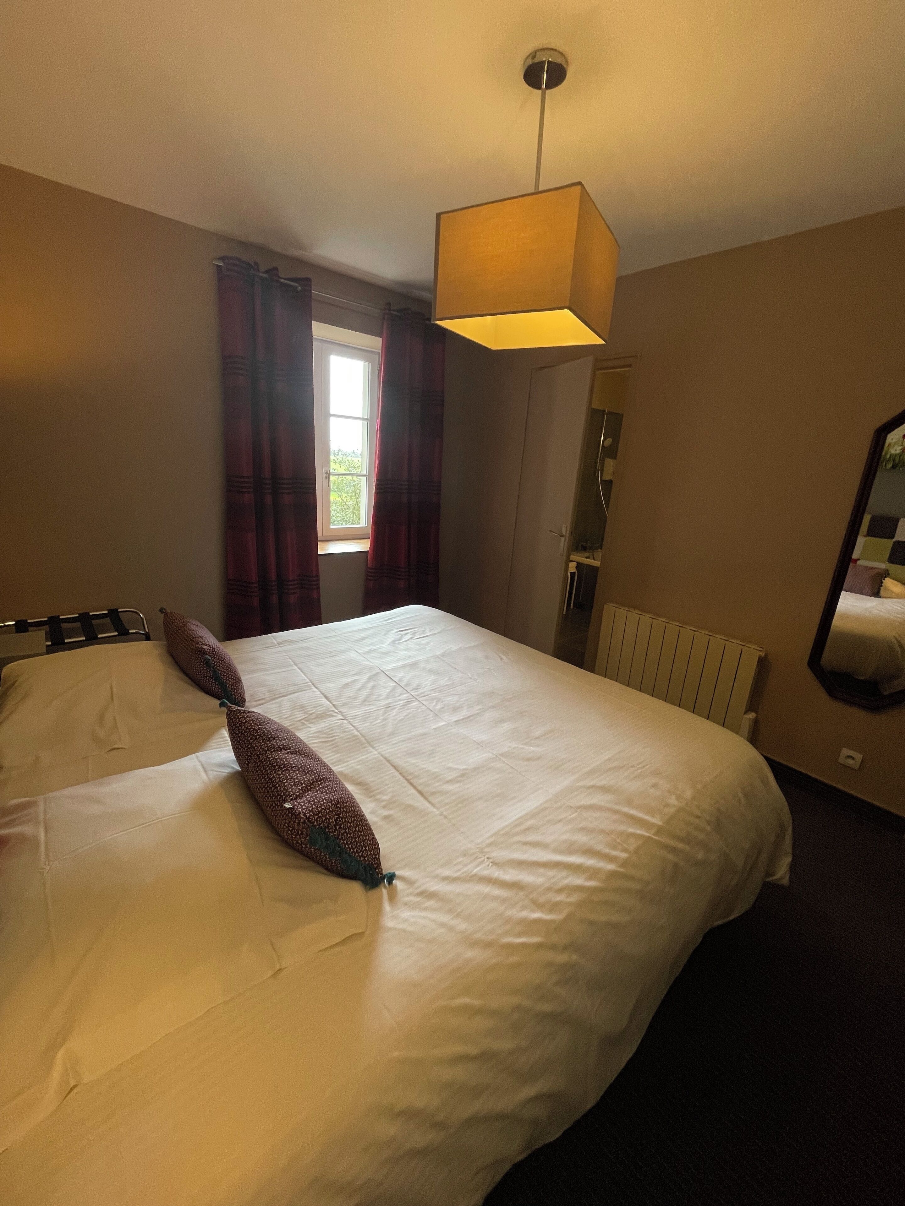 A hotel room with a large bed, a window with curtains, a radiator, and a mirror on the wall.