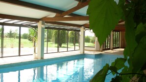 An indoor swimming pool with a glass ceiling, surrounded by potted plants and a view of a green landscape. - Domaine du Griffier (Granzay-Gript)