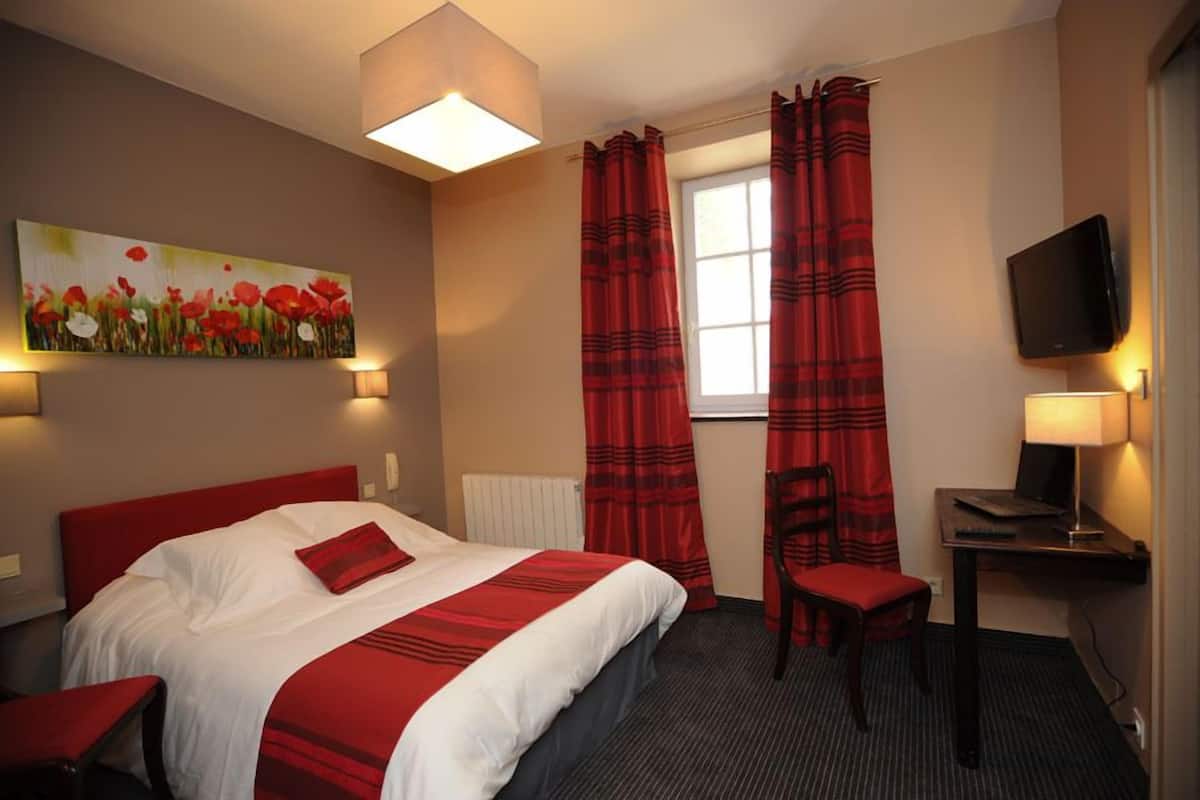 A hotel room with a bed, a desk with a chair, a TV, and a painting on the wall.