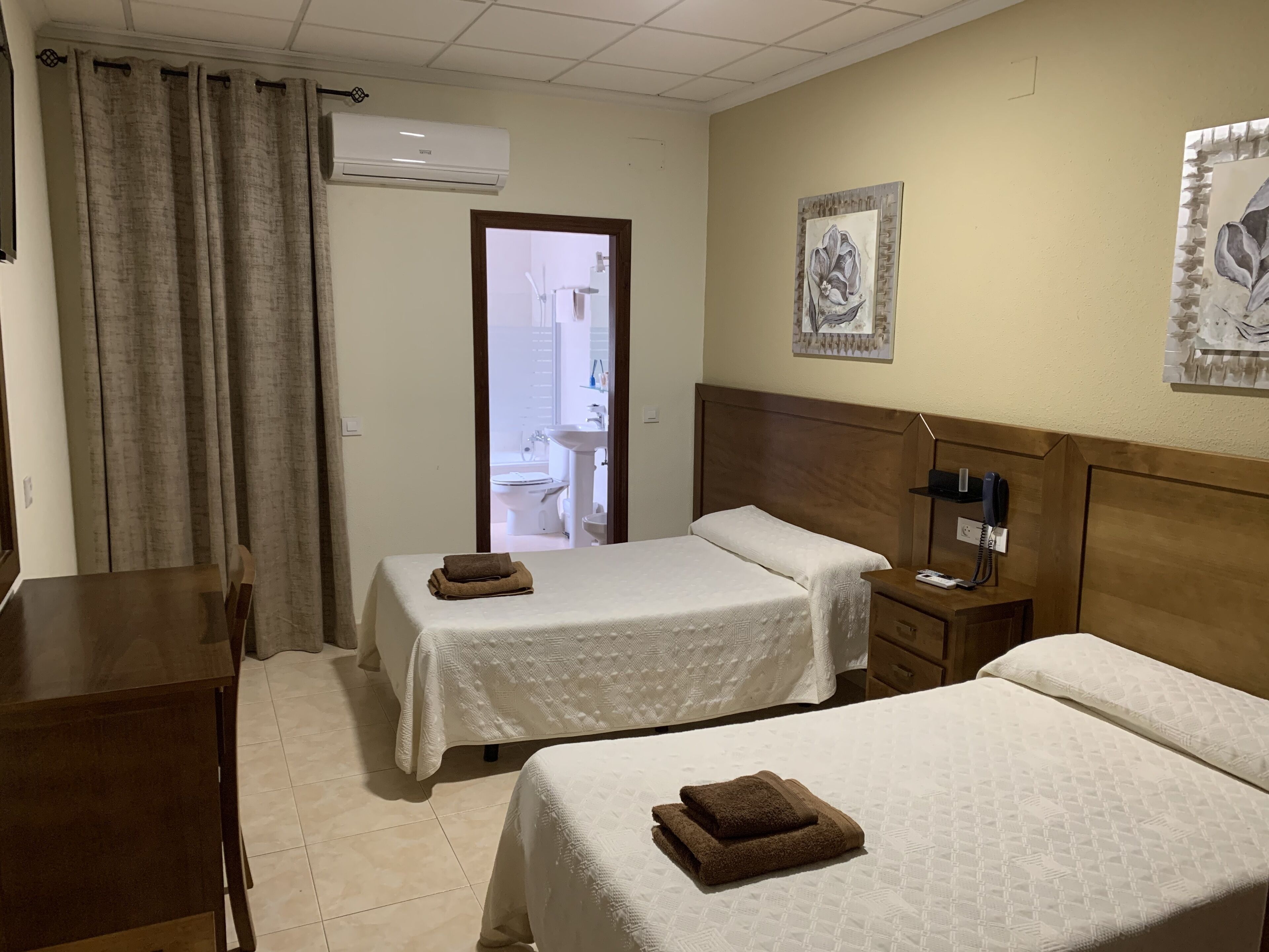 Ein Hotelzimmer mit zwei Betten, einem Schreibtisch, einem Stuhl, einem Nachttisch mit Telefon und einem Bild an der Wand.