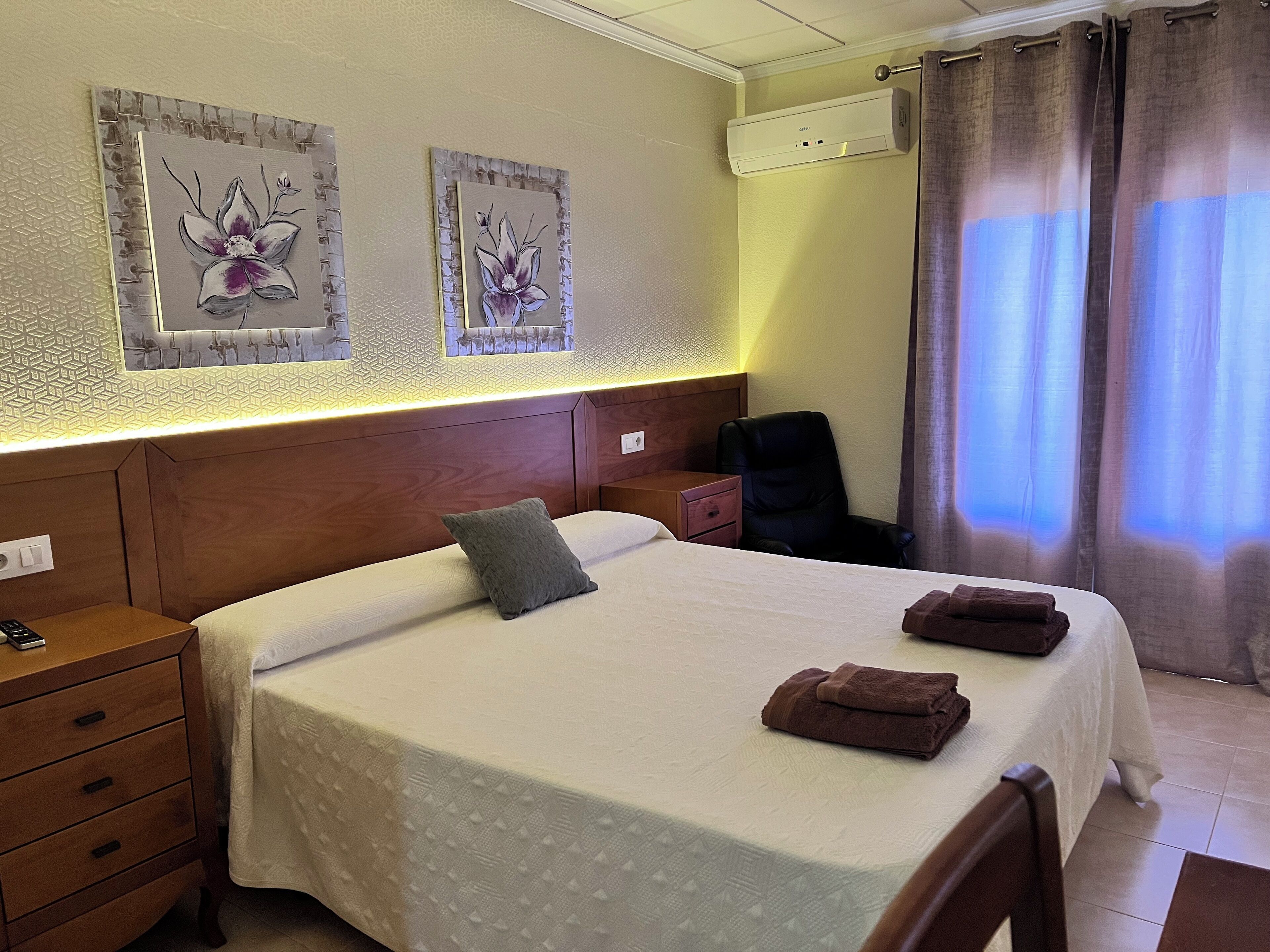 Un cuarto de hotel con una cama grande, una mesita de noche, una silla y obras de arte en la pared.