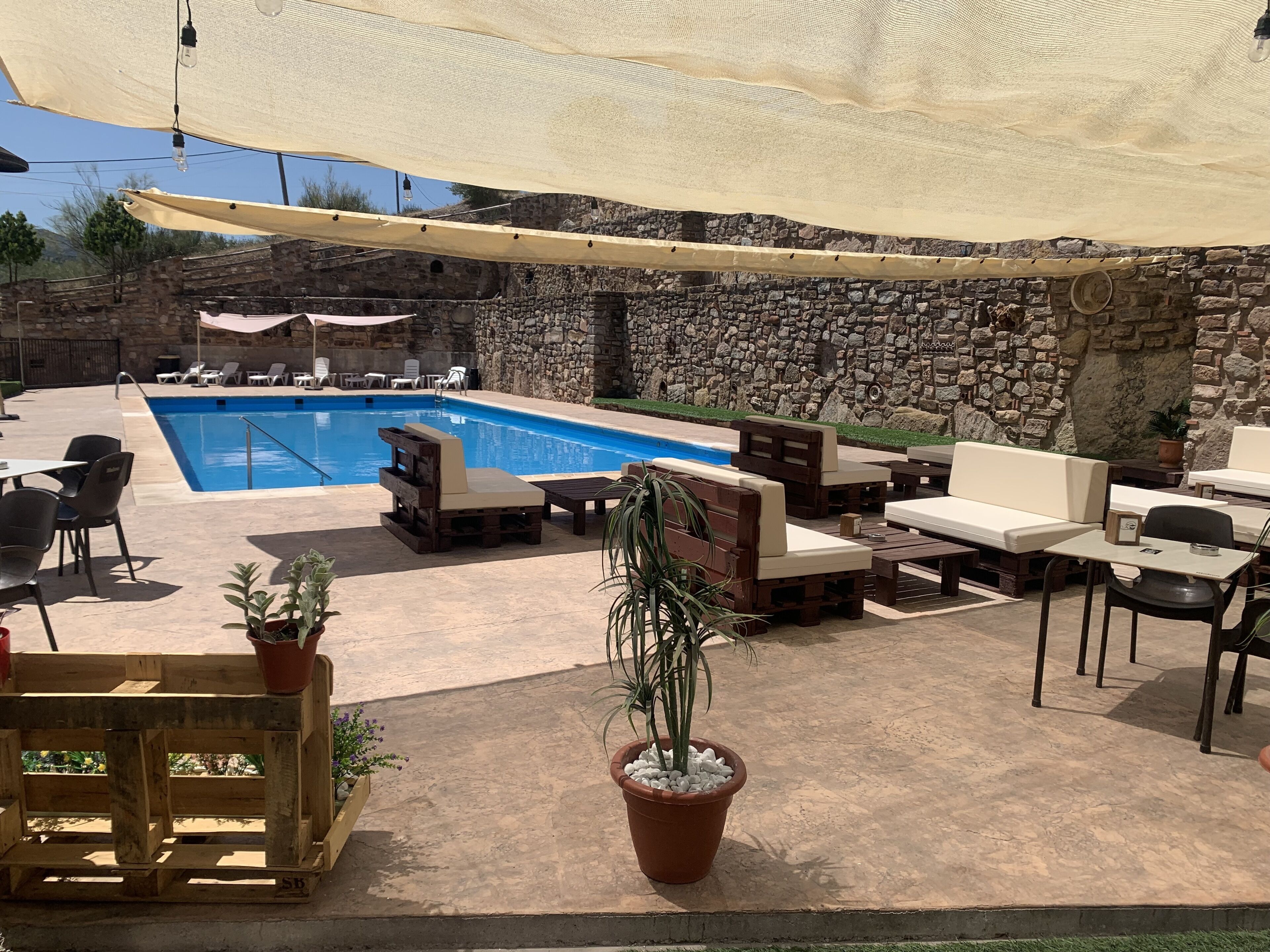 Un área de piscina con muros de piedra, mobiliario de madera y plantas en macetas.